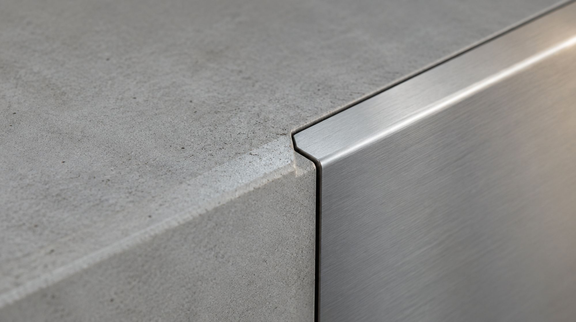 Macro detail of architectural concrete meeting a brushed stainless steel edge trim.