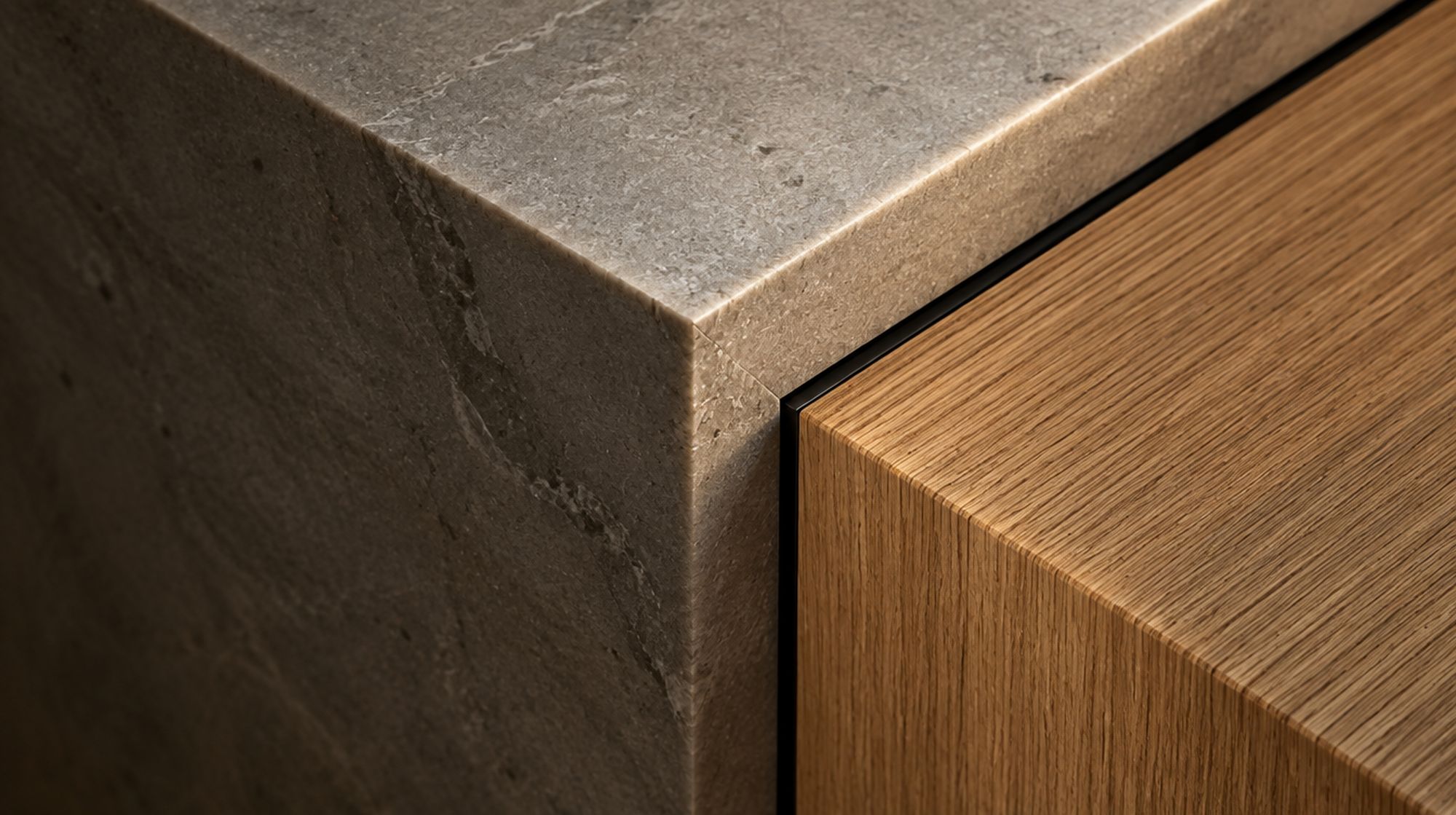 Macro detail of a mitered corner where honed stone meets rift-sawn white oak with a fine blackened metal reveal between them.